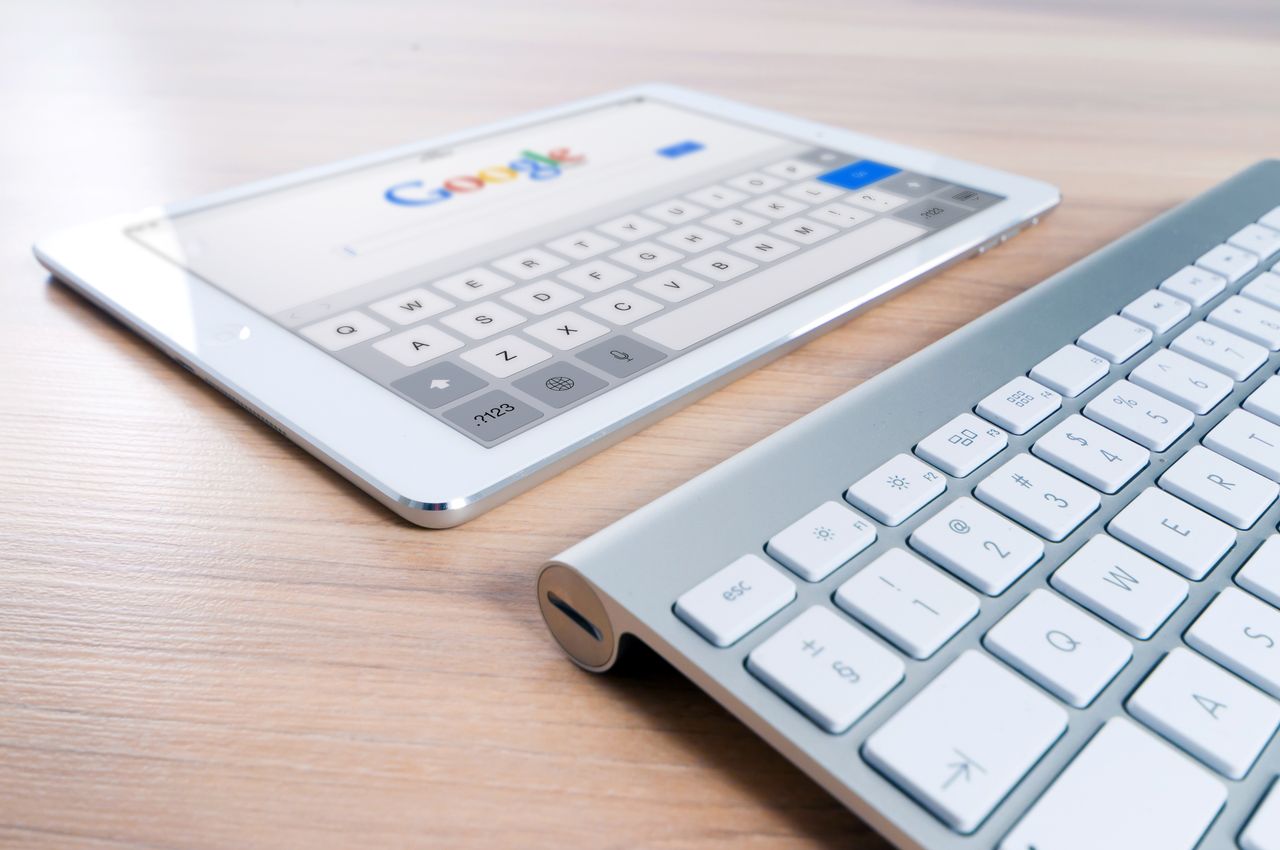 Une tablette moderne affichant le logo d'un moteur de recherche à côté d'un clavier sans fil posé sur un bureau en bois.